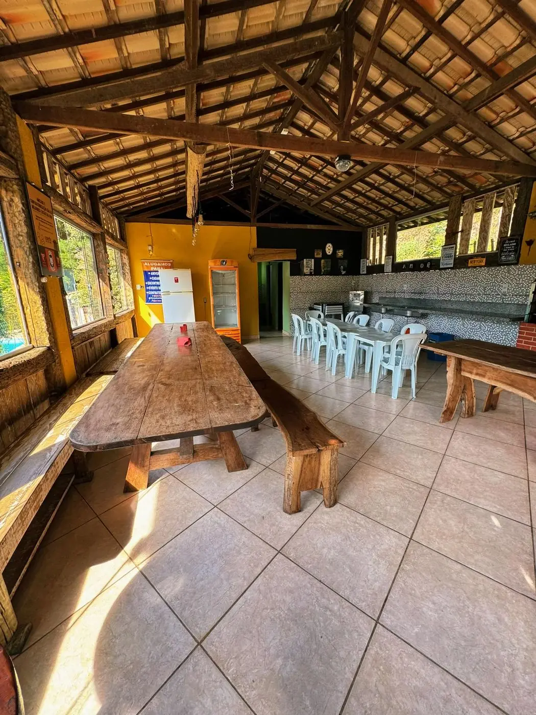 Confraria: salão coberto com mesas longas de madeira e churrasqueira