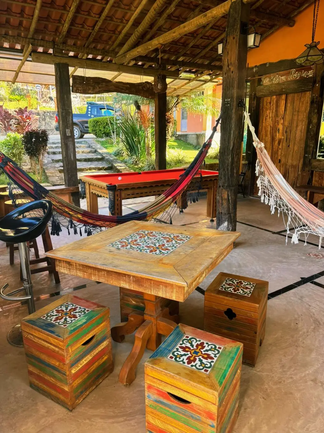 Área de jogos com redes armadas, mesa de sinuca e banquinhos de azulejo